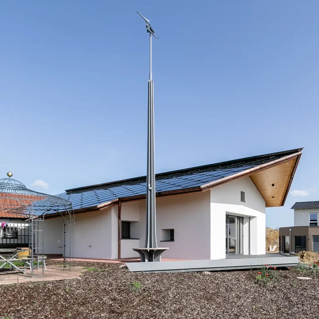 Modernes weißes Einfamilienhaus mit geneigtem Dach und schwarzem Elektroauto unter Carport.