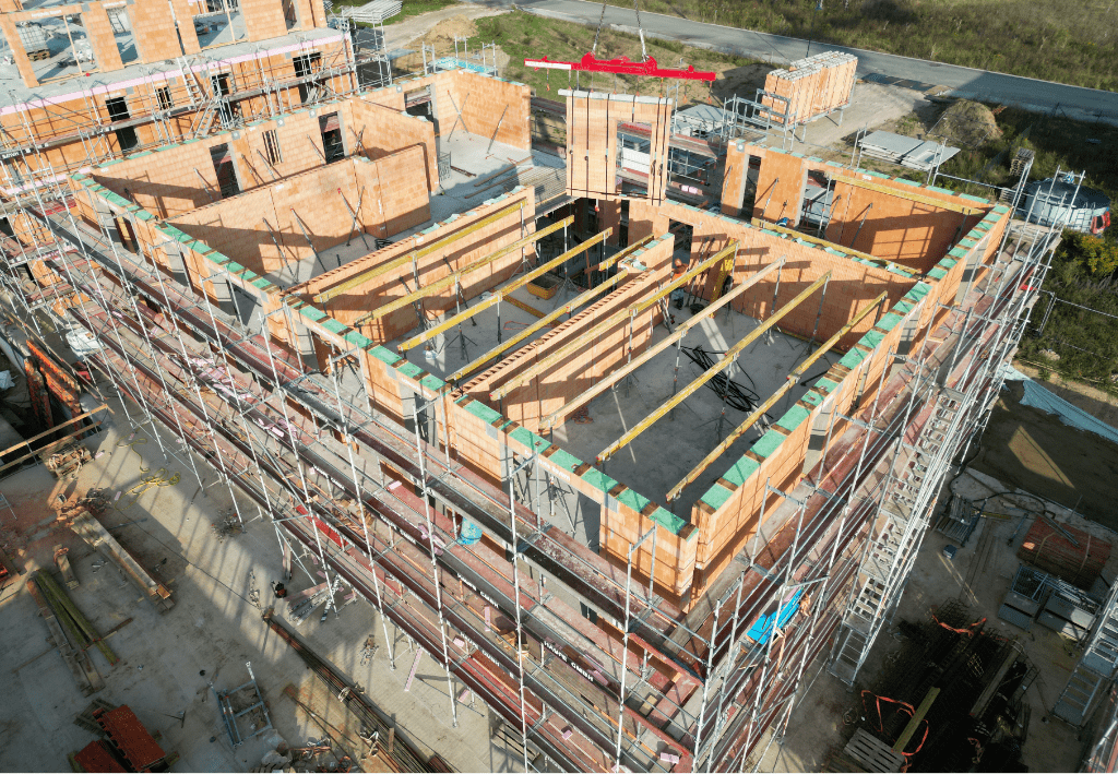Bau eines mehrstöckigen Gebäudes mit Holzrahmen und Gerüst, umgeben von Baustellenmaterialien.