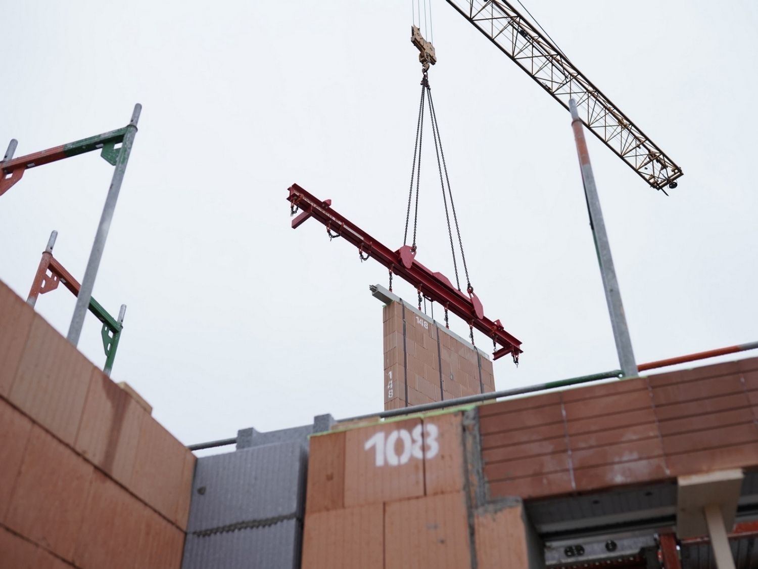 Kran hebt eine große Ziegelfertigteilwand über eine Baustelle einer Wohnanlage in Werneuchen.